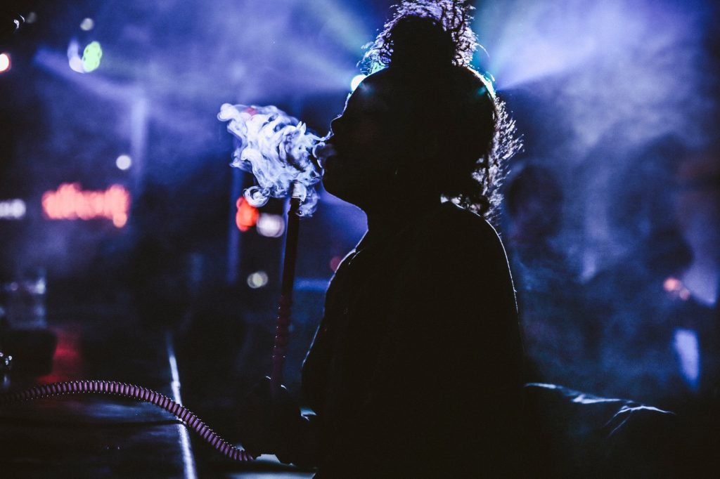 Young lady smoking hookah shisha pipe in a busy cafe