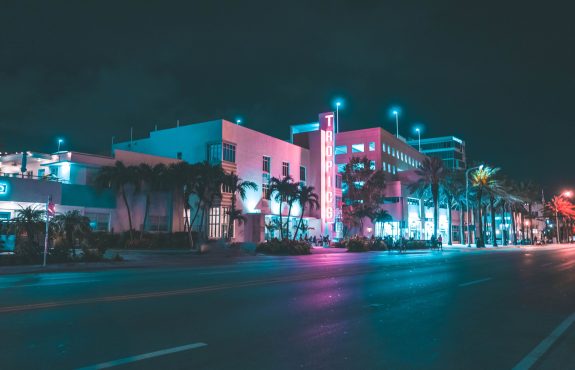 Night street scene of Miami with pink and blue neon lights.
